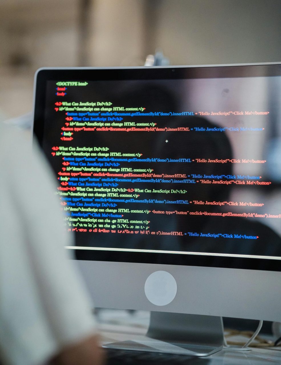 A close-up of a computer screen displaying colorful coding script in an office environment.